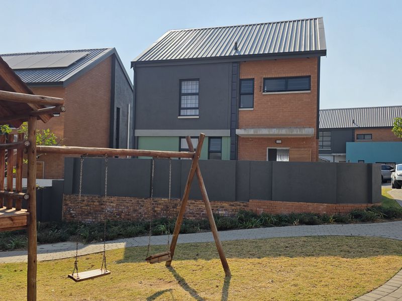 Rear view of a modern townhouse featuring a combination of brick and rendered finishes, a corrugated metal roof, and a private boundary wall.