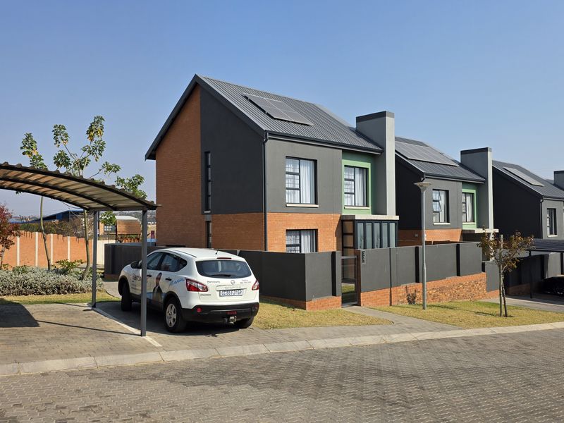 Modern townhouse exterior featuring a brick and painted facade, solar panels, and a dedicated carport in a well-maintained residential complex.