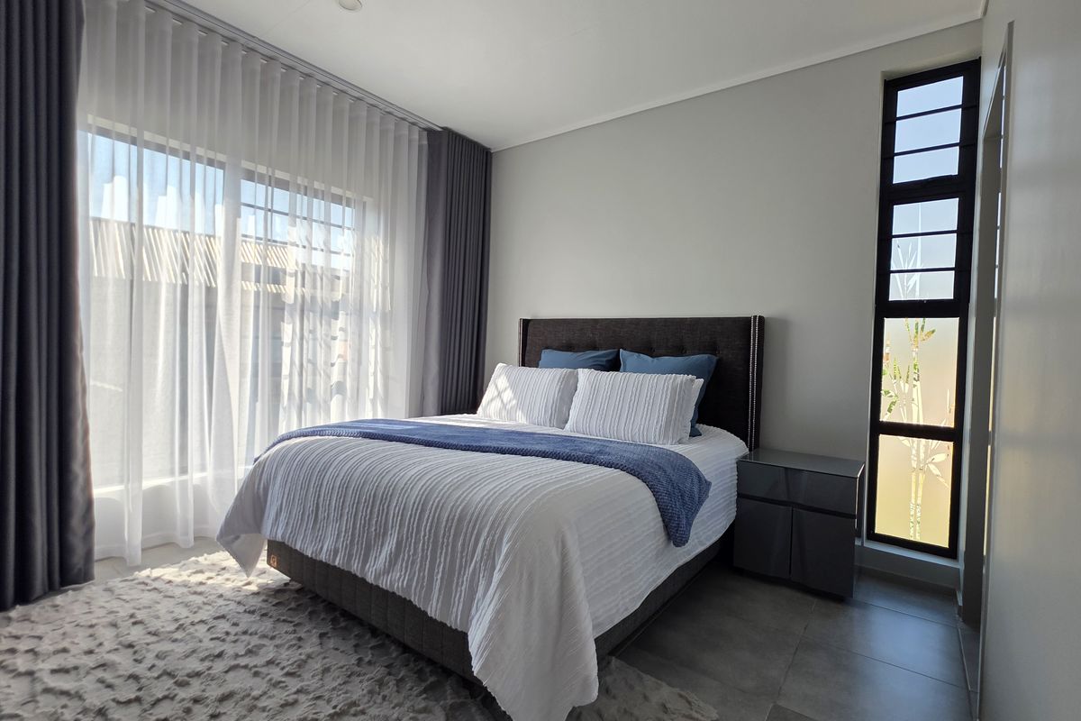 A bright and modern bedroom featuring large sliding glass doors, a vertical window, tiled flooring, and neutral wall finishes.
