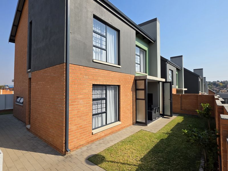 Rear view of a modern townhouse featuring a combination of brick and rendered facade, paved walkway, small lawn, and secure boundary wall with electric fencing.