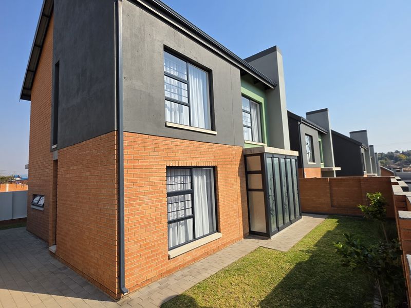 Rear view of a modern townhouse featuring a combination of face brick and plastered finishes, aluminium window frames, and a paved garden area.
