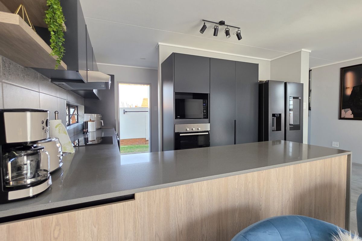 Modern kitchen featuring sleek dark cabinetry, quartz countertops, integrated appliances, and a breakfast bar, with direct access to the rear exterior.
