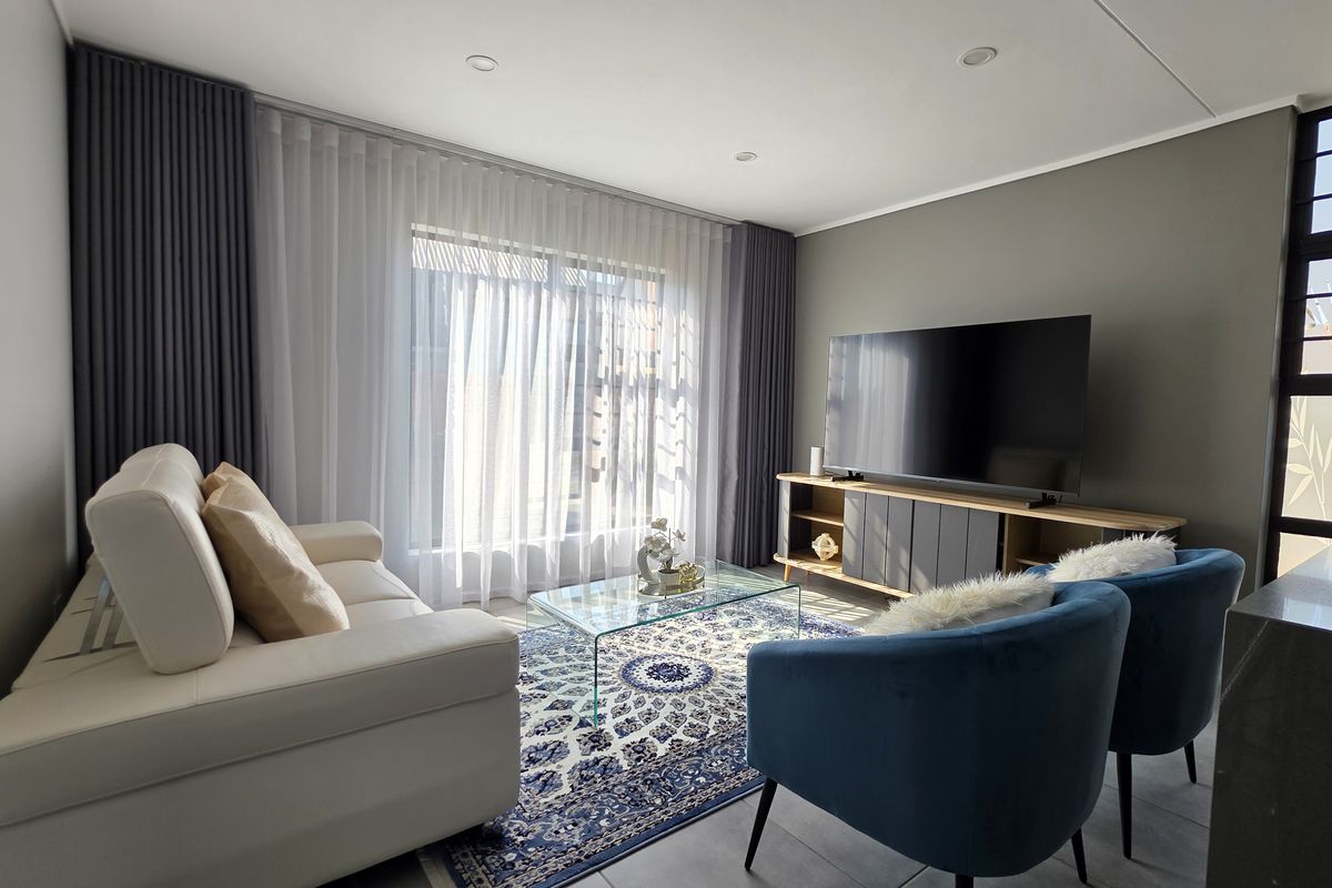 A modern, well-lit living room featuring tiled flooring, recessed downlighting, and large windows with integrated curtain tracks, creating a bright and comfortable living space.