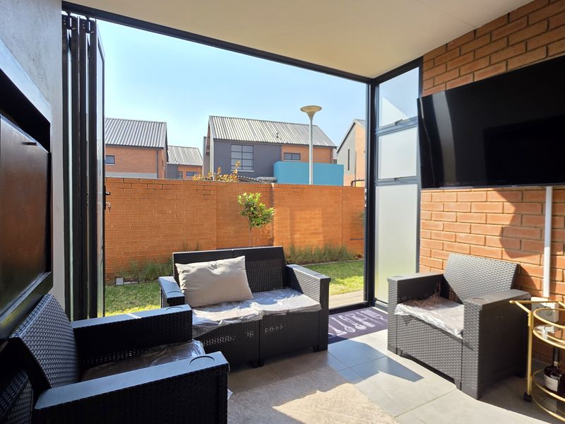 A covered patio area featuring exposed brick walls, tiled flooring, and large folding glass doors that open onto a private garden space.