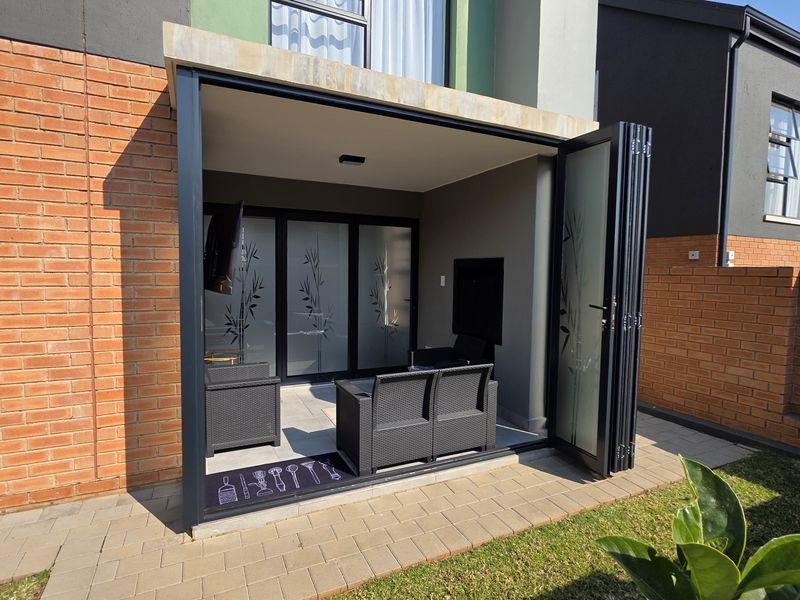 A modern covered patio featuring sleek stacking glass doors, brick exterior walls, and paved flooring, providing a seamless transition to the garden area.