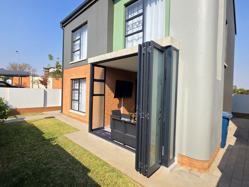 Rear view of the townhouse featuring a paved patio area with modern stacking doors, brick exterior finishes, and a private garden space.