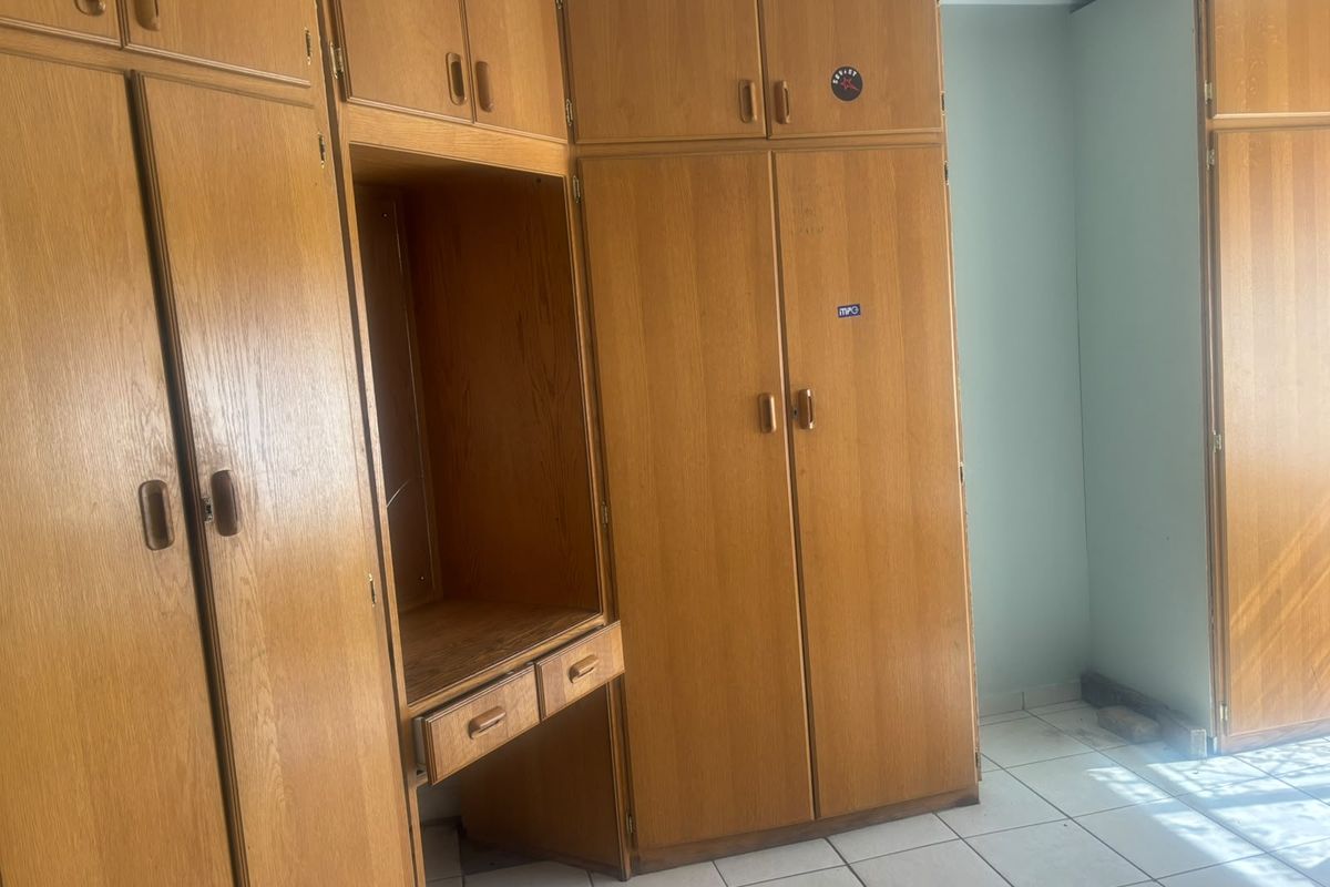 A bedroom featuring extensive built-in wooden cabinetry with integrated desk space and tiled flooring, offering significant storage potential.