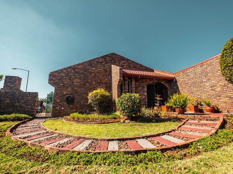 A well-maintained face brick house featuring a charming curved paved garden path and a secure wrought iron entrance gate.