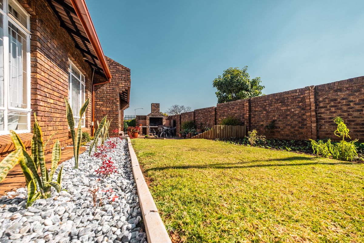 A well-maintained rear garden featuring a brick boundary wall, a lawn area, and a built-in outdoor braai facility.