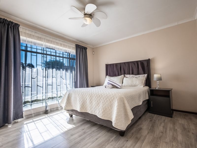 A well-maintained bedroom featuring light-toned laminate flooring, a ceiling fan, and large windows fitted with security bars.