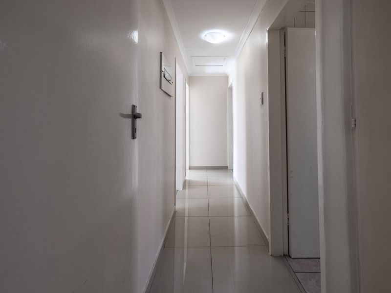 A clean, neutral hallway featuring tiled flooring and multiple internal access points, providing a bright and functional transition space within the home.