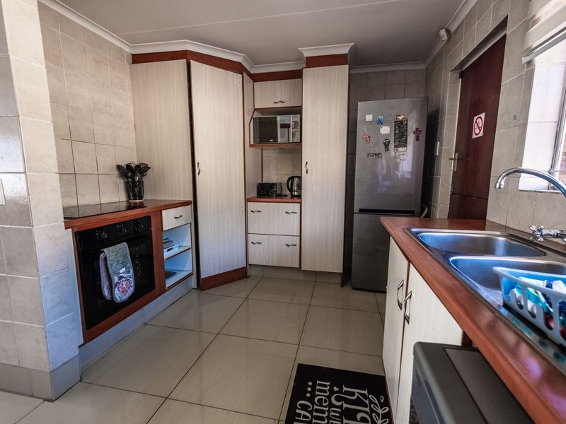 A functional kitchen featuring built-in cabinetry, an integrated oven and hob, tiled splashbacks, and a double bowl sink with tiled flooring.