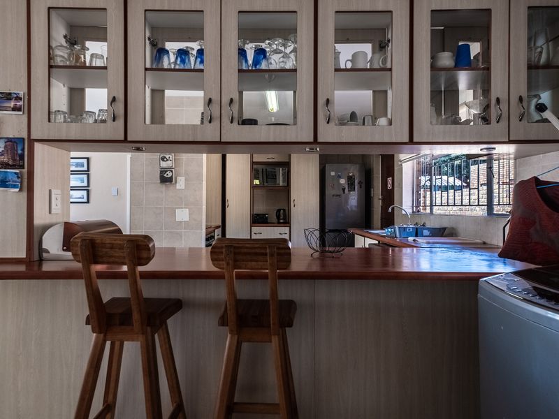A functional kitchen featuring timber breakfast bar countertops, glass-fronted cabinetry, and a tiled backsplash, offering a practical layout for daily use.