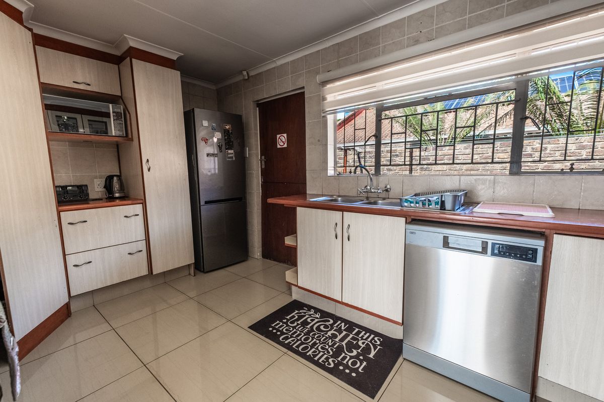 Functional kitchen featuring light-toned cabinetry, tiled backsplash, double basin sink, and integrated dishwasher with tiled flooring throughout.