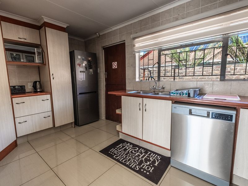 Functional kitchen featuring light-toned cabinetry, tiled backsplash, double basin sink, and integrated dishwasher with tiled flooring throughout.