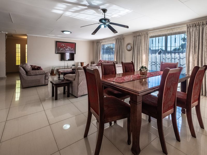 Spacious open-plan living and dining area featuring polished tiled flooring, a ceiling fan, and large sliding glass doors with security bars.