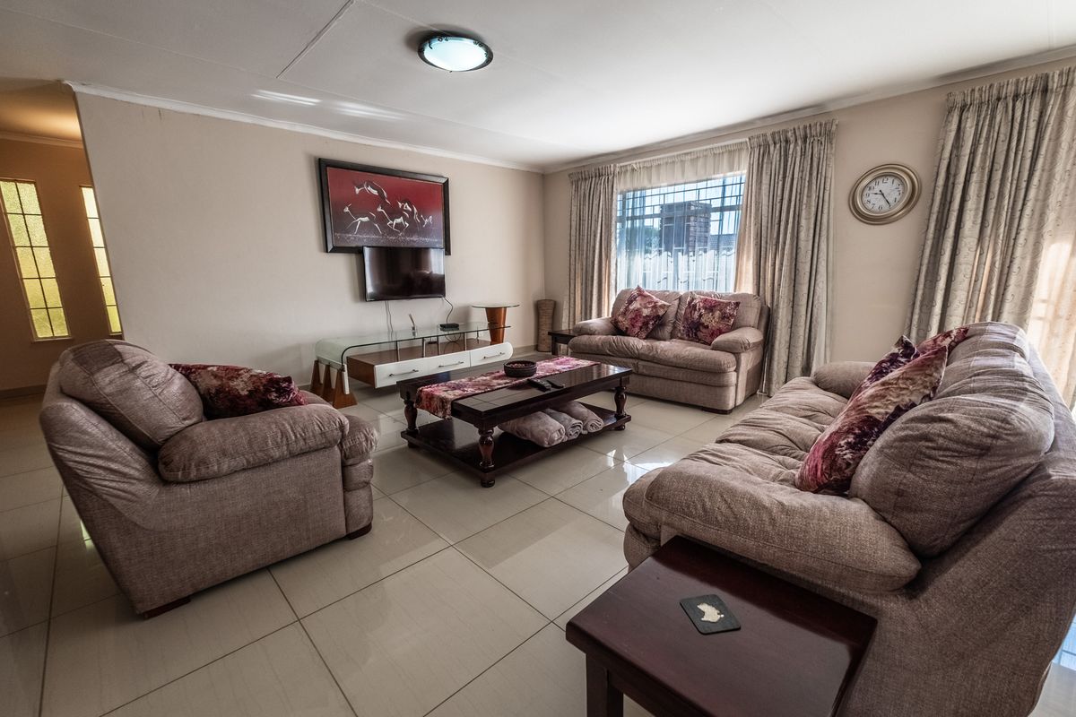 A spacious living room featuring large floor tiles, neutral wall tones, and natural light through window curtains.
