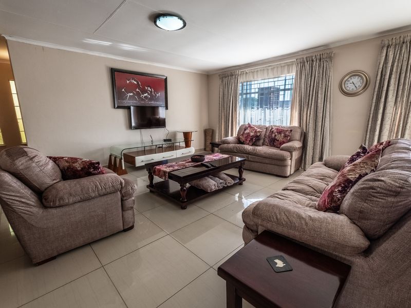 A spacious living room featuring large floor tiles, neutral wall tones, and natural light through window curtains.