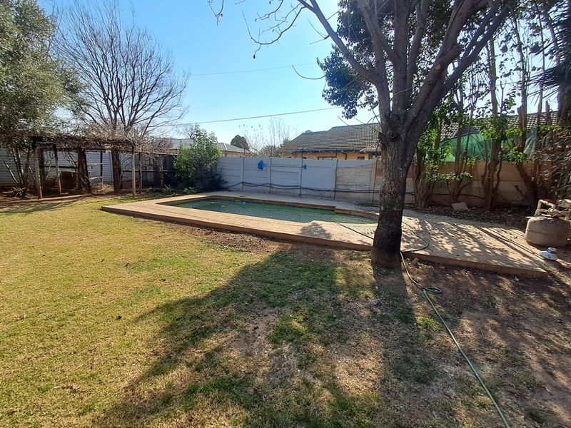Backyard area featuring a swimming pool with paved surround, a precast boundary wall, and a pergola structure in a garden setting.