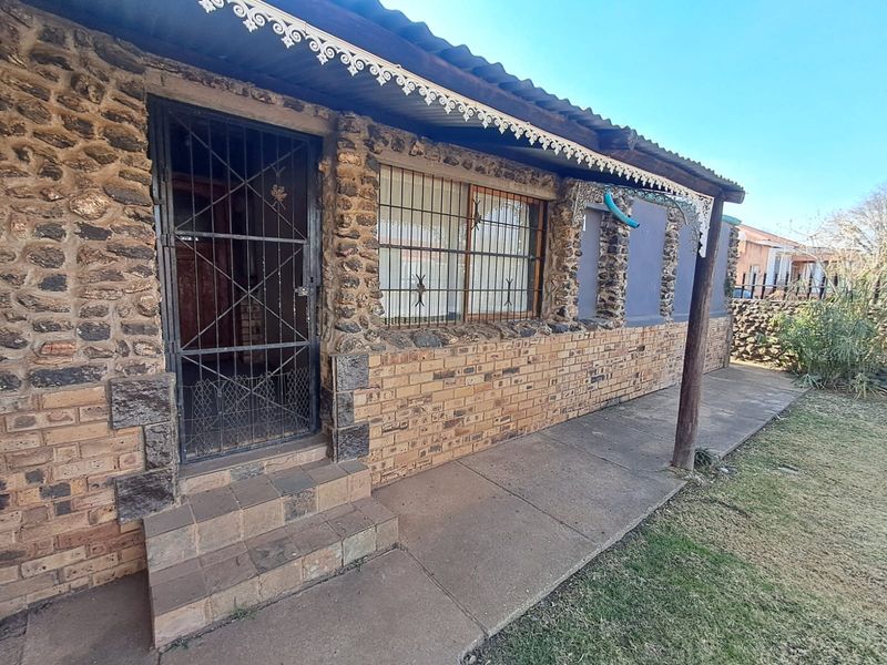 Front facade of a house featuring stone and face brick construction, security gates, and a covered walkway.
