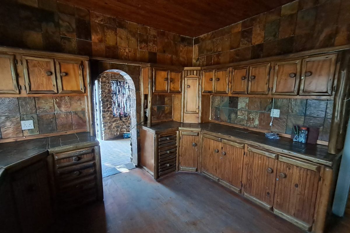 A rustic kitchen featuring extensive wooden cabinetry, stone tile backsplashes, and a distinctive stone archway leading to an adjacent area.