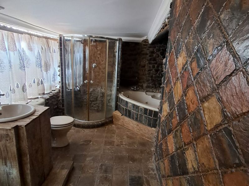 A rustic-style bathroom featuring a corner shower, built-in bathtub, and distinctive stone tile wall and floor finishes.