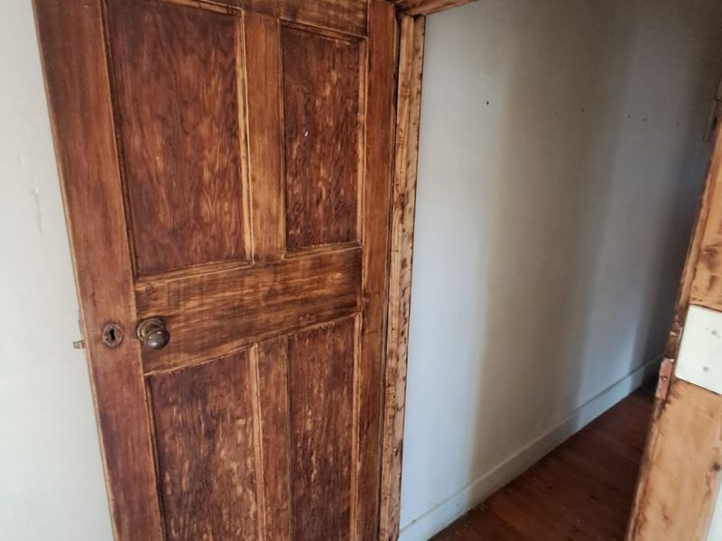 A narrow hallway featuring original timber flooring and a rustic wooden door with an unfinished door frame.
