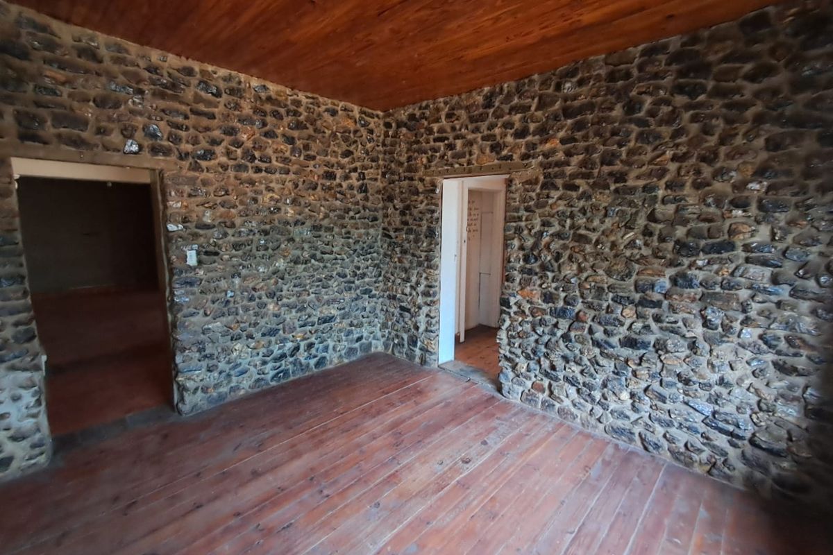 An empty living area featuring rustic exposed stone walls, a timber-clad ceiling, and original timber flooring, offering a unique character-filled space.