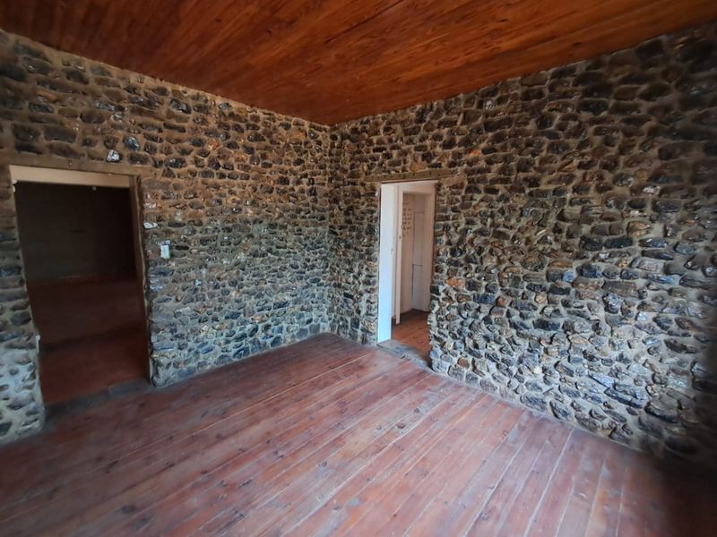 An empty living area featuring rustic exposed stone walls, a timber-clad ceiling, and original timber flooring, offering a unique character-filled space.