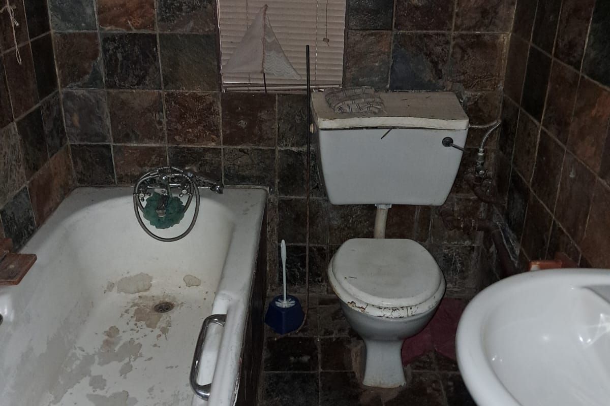 A dated bathroom featuring a pedestal basin, toilet, and bathtub with stone-tiled walls, requiring significant refurbishment and modernization of fixtures and finishes.
