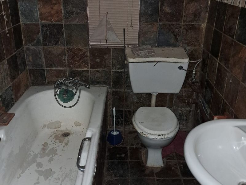 A dated bathroom featuring a pedestal basin, toilet, and bathtub with stone-tiled walls, requiring significant refurbishment and modernization of fixtures and finishes.