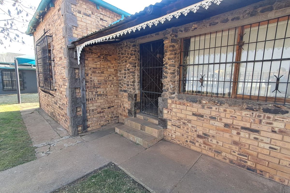 Front exterior view of a face brick house featuring stone masonry accents, security bars on windows, and a concrete walkway.