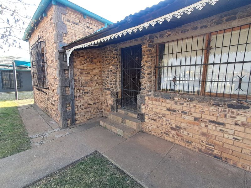 Front exterior view of a face brick house featuring stone masonry accents, security bars on windows, and a concrete walkway.