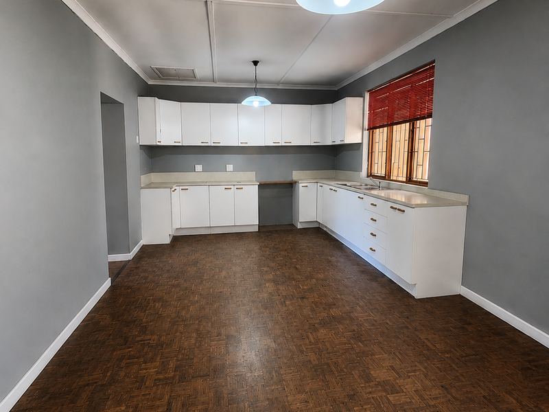 Spacious kitchen featuring white built-in cabinetry, laminate countertops, a double basin sink, and classic parquet flooring, offering a clean and functional layout.