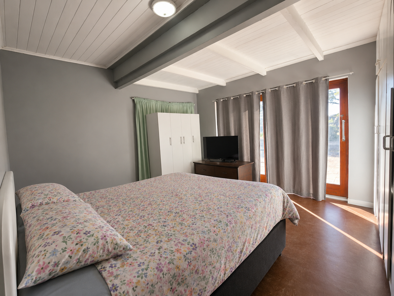 A bedroom featuring exposed ceiling beams, built-in wardrobe storage, and direct access to an outdoor area through a timber door.