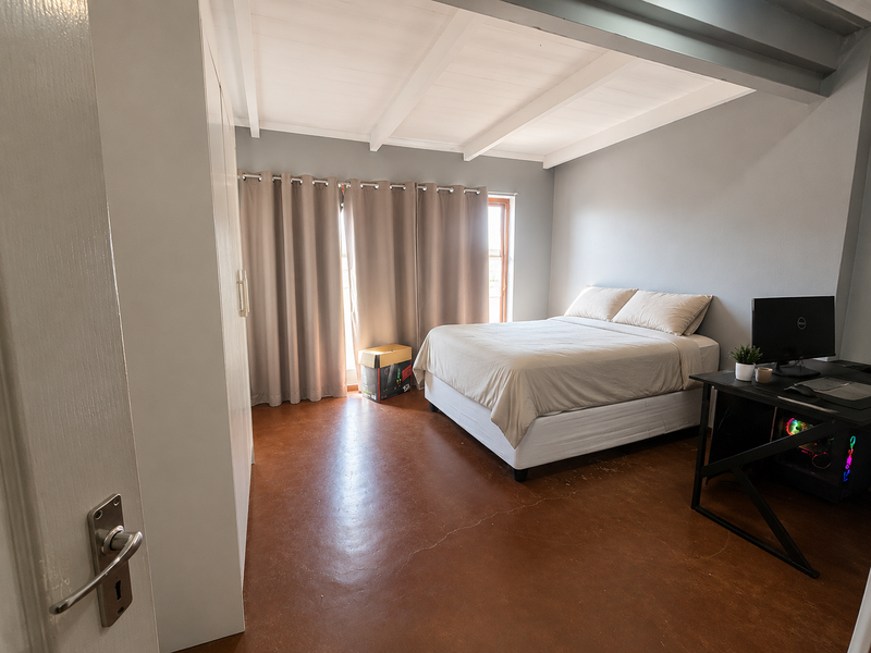 A well-maintained bedroom featuring polished concrete floors, exposed timber ceiling beams, and a built-in wardrobe, offering a clean and functional living space.