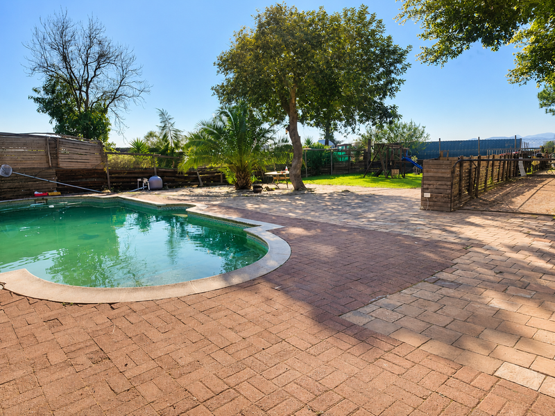 Outdoor pool area featuring a paved patio, timber perimeter fencing, and a swimming pool requiring maintenance.