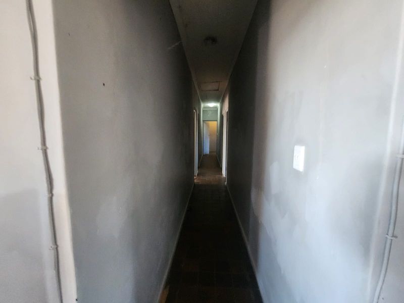 A narrow, dimly lit hallway featuring tiled flooring and visible surface-mounted electrical conduits, requiring cosmetic updates to improve the overall aesthetic.