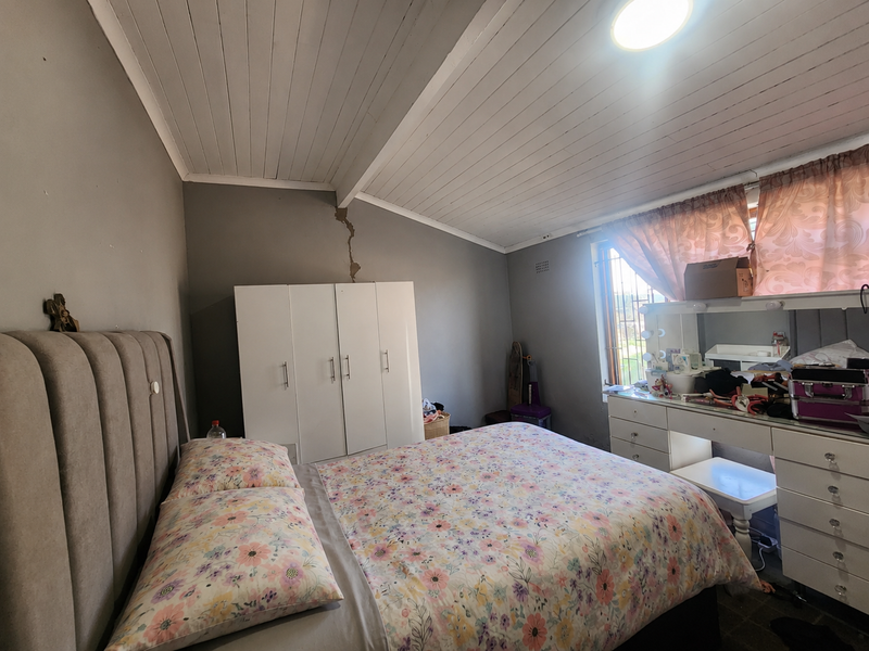 A bedroom featuring a timber-clad ceiling and a window with security bars. The room shows signs of structural wall cracking.