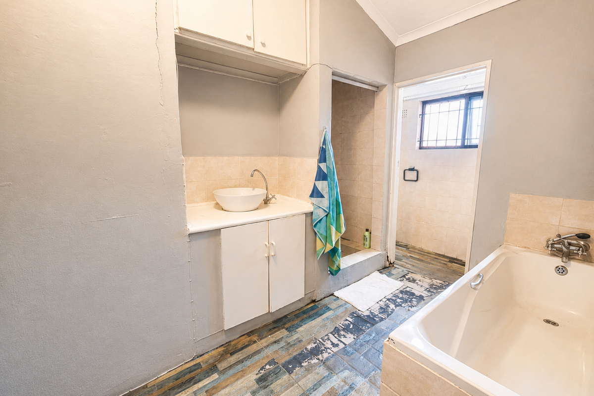 A dated bathroom featuring a vanity with vessel sink, a bathtub, and a separate shower area, requiring cosmetic updates and floor repairs.