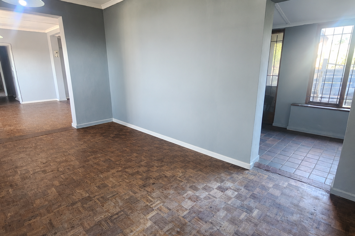 An empty living area featuring classic parquet flooring, neutral grey walls, and direct access to adjacent rooms and a tiled entryway.