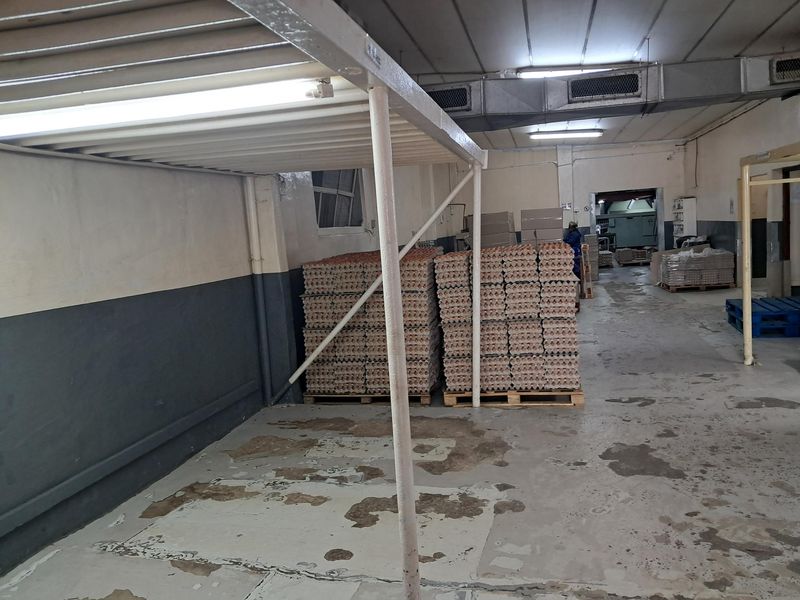 A functional utility or storage space featuring exposed industrial ducting, fluorescent lighting, and durable concrete flooring, currently used for bulk storage.