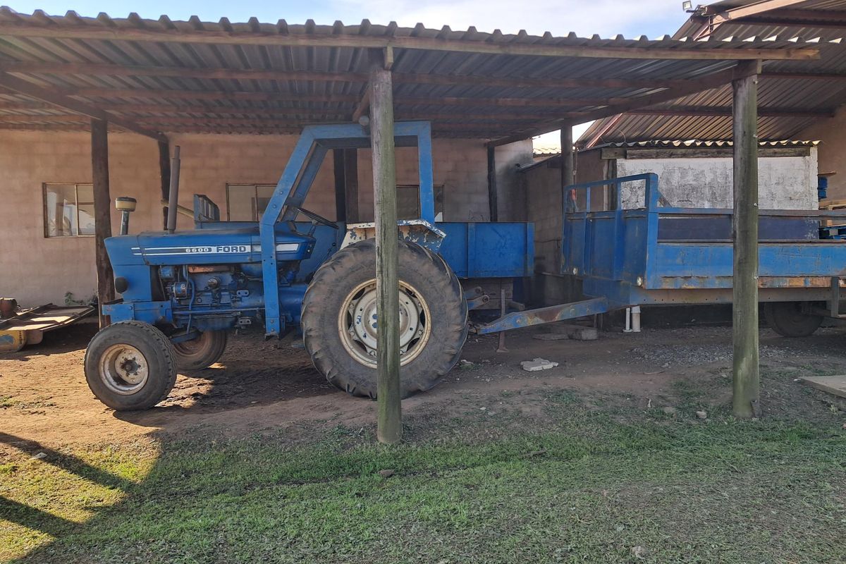 A covered outdoor utility area with a corrugated iron roof and timber support posts, currently used for storage of farm equipment.
