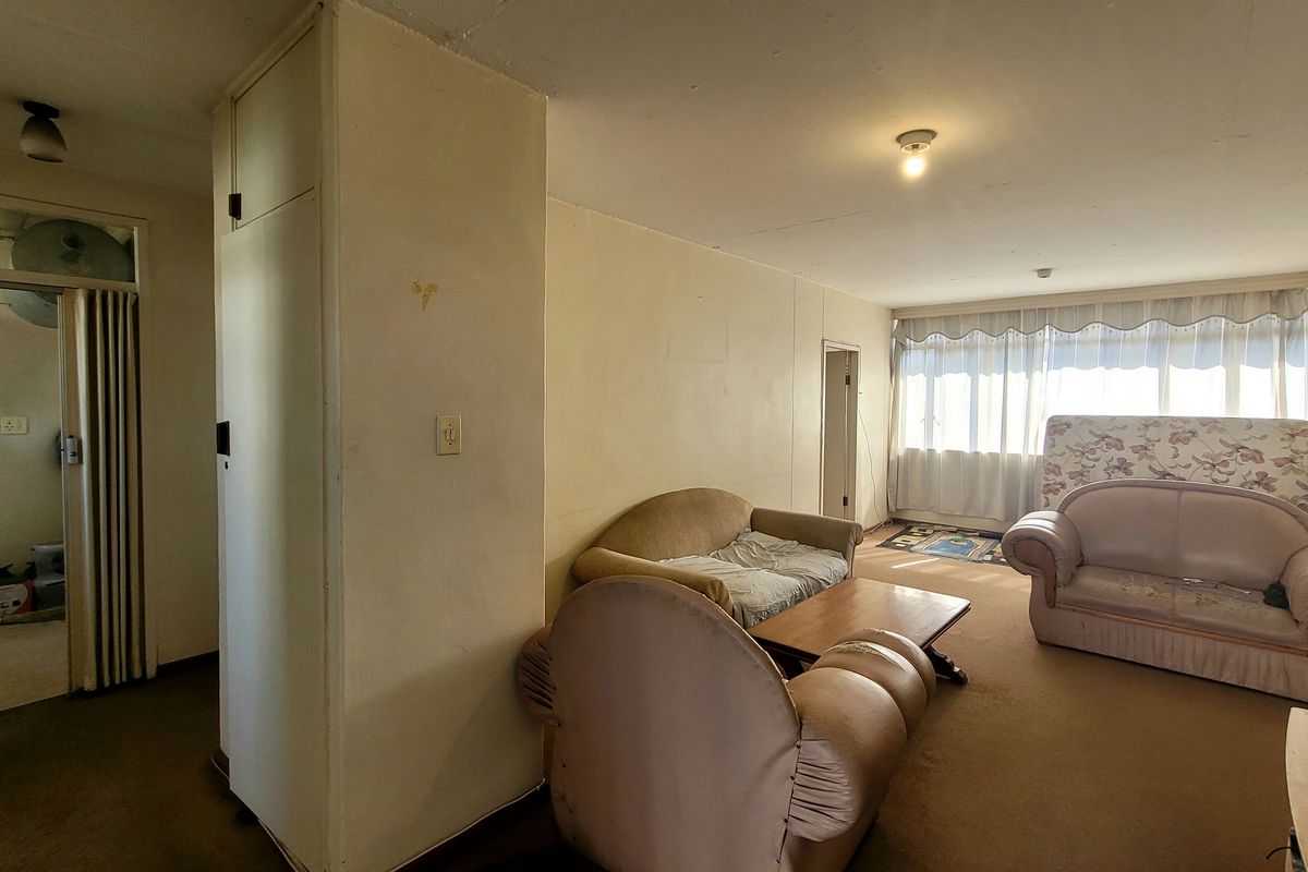 Spacious living area featuring a built-in cupboard, folding door access, and large windows allowing for natural light, requiring cosmetic updates to finishes.