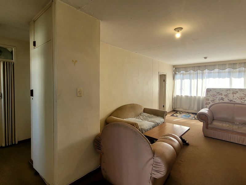 Spacious living area featuring a built-in cupboard, folding door access, and large windows allowing for natural light, requiring cosmetic updates to finishes.