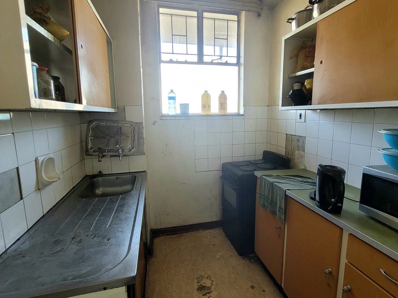 A compact, dated kitchen featuring original cabinetry, a stainless steel sink, and a freestanding stove, requiring modernization and cosmetic updates.