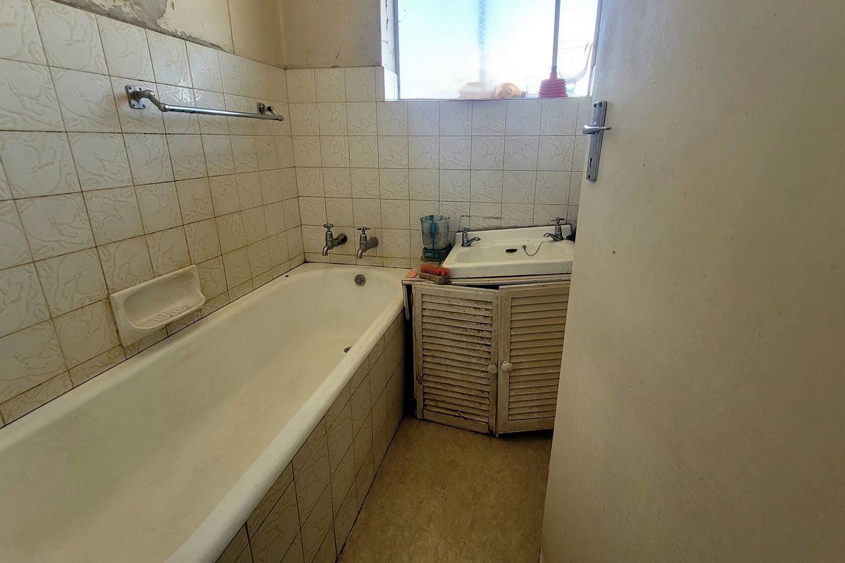A dated bathroom featuring a standard bathtub, wall-mounted basin with vanity cabinet, and tiled wall finishes requiring renovation.