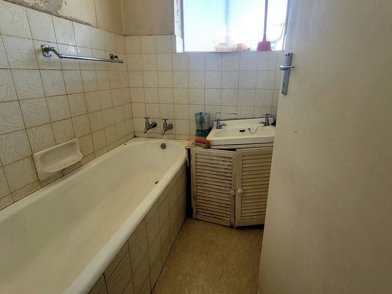 A dated bathroom featuring a standard bathtub, wall-mounted basin with vanity cabinet, and tiled wall finishes requiring renovation.