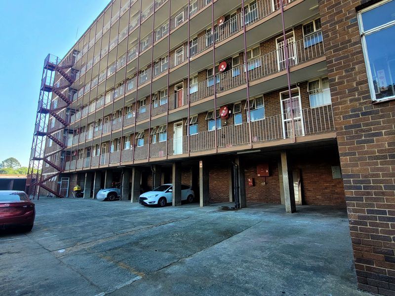 Exterior view of a multi-story brick apartment building featuring a metal fire escape, private balconies, and a ground-level covered parking area.