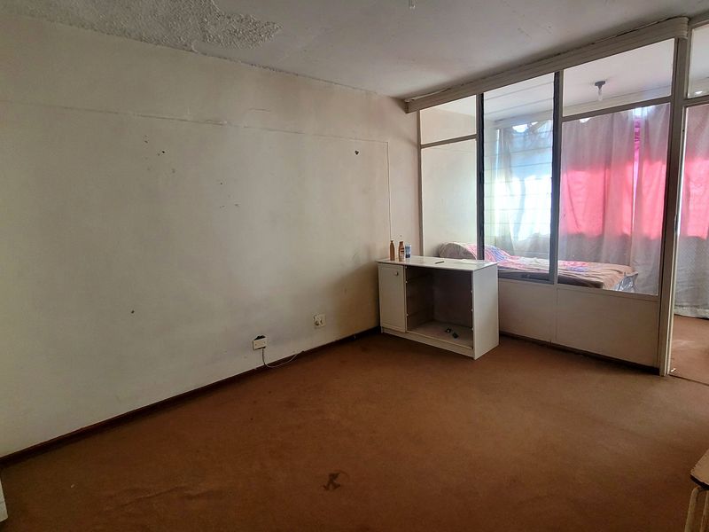 A bedroom featuring a glass partition wall and carpet flooring, requiring cosmetic updates and repairs to the walls and ceiling.